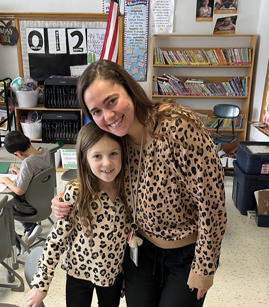 A teacher hugs an elementary aged student who is wearing matching clothing - a leopard print shirt and leggings.