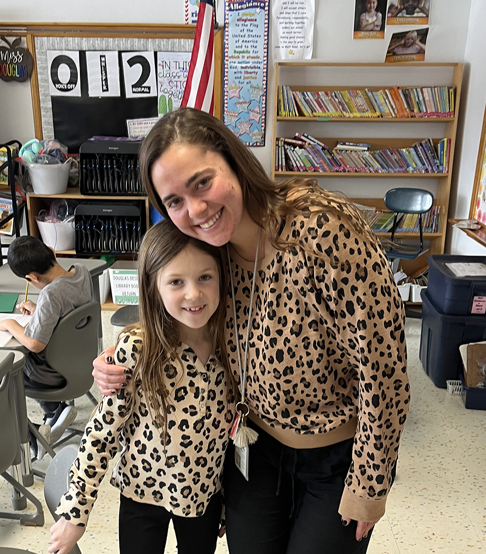 A teacher hugs an elementary aged student who is wearing matching clothing - a leopard print shirt and leggings.