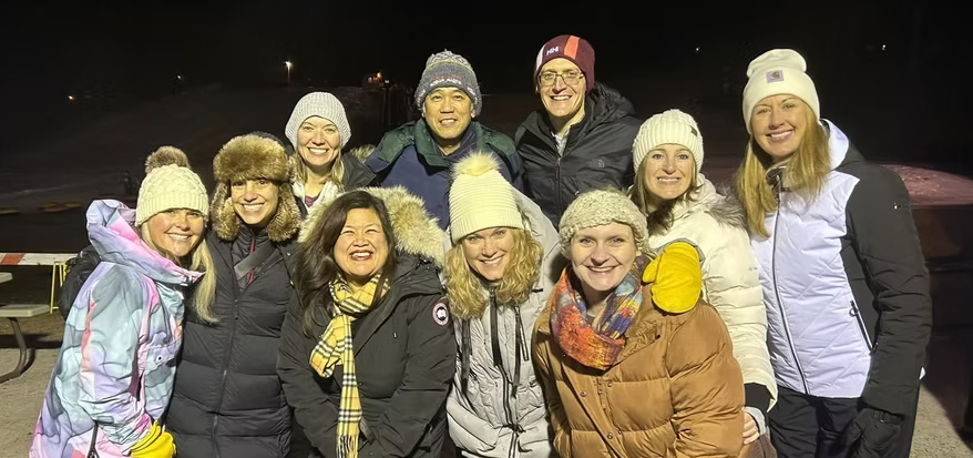 Several parents dressed warm huddle together outside in a nighttime winter setting.