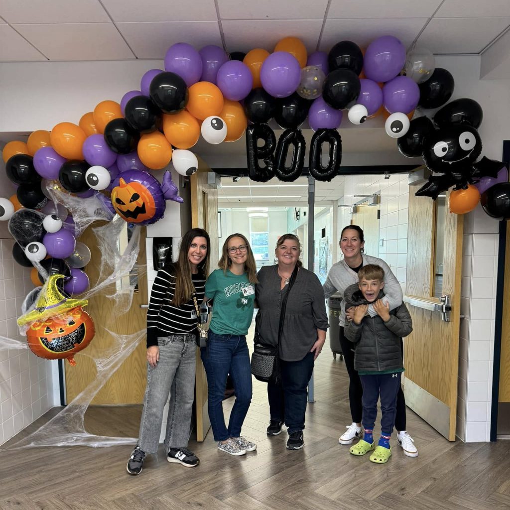 Several HSA parents gather with a child in the doorway decorated for a Halloween party.