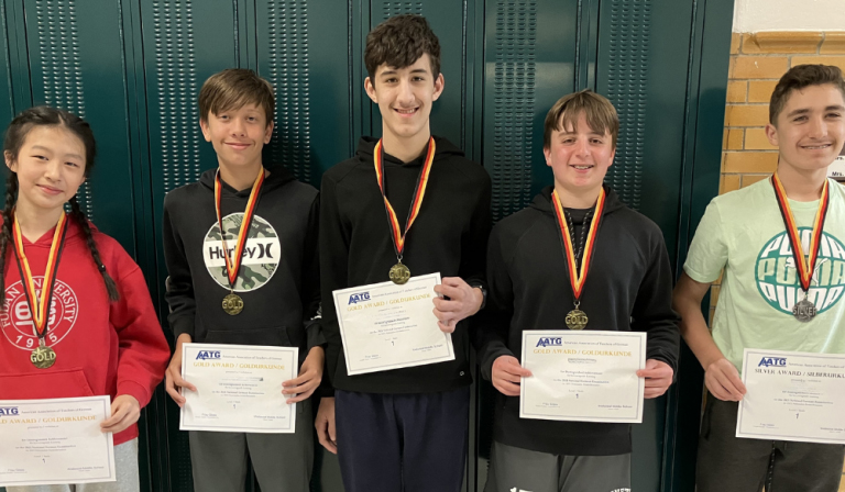 Five students stand in front of lockers displaying certificates and medals.