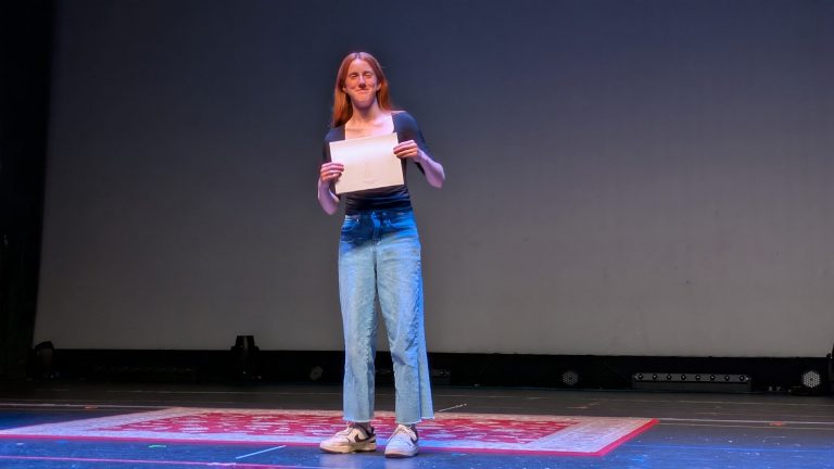 A student proudly clutches a certificate on a stage.