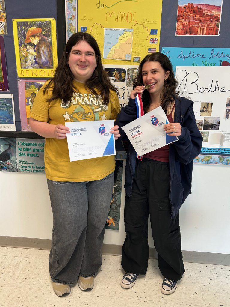 Two high school students display their certificates in a classroom setting.