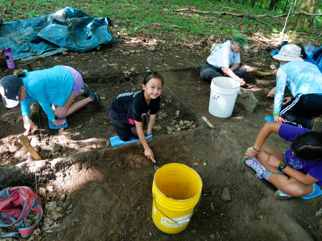 Student smiles at camera while digging in dirt for artifacts.