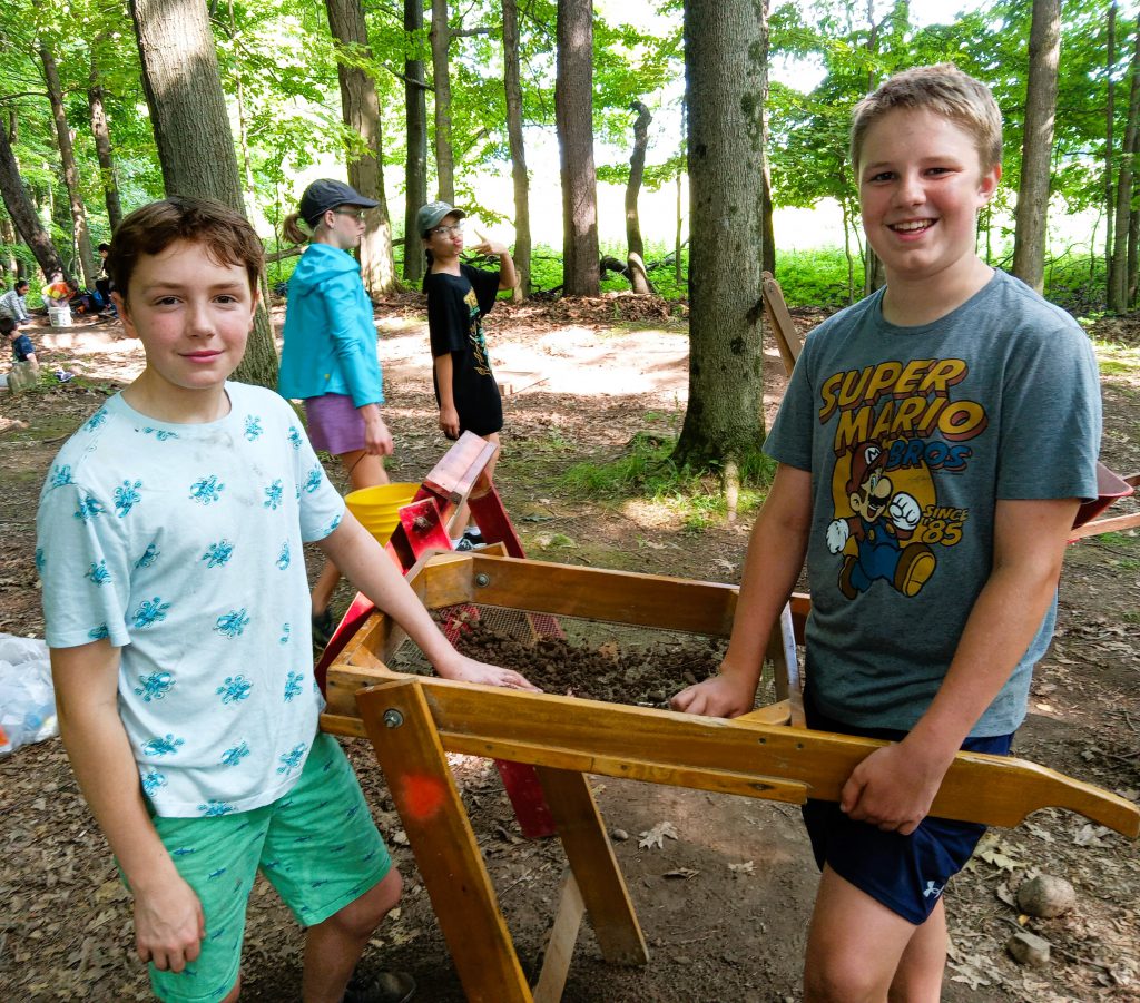 Students smile at camera while sifting dirt.