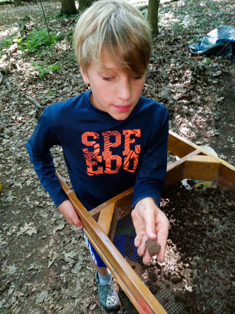 Student looks at item found while sifting dirt.