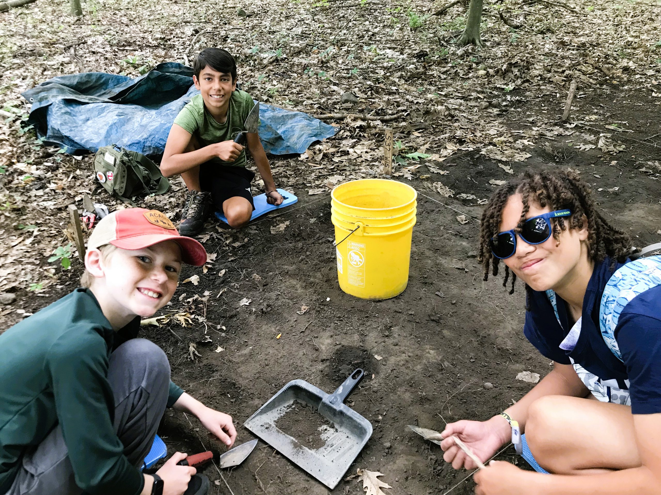 Students smile towards camera while digging up artifacts.