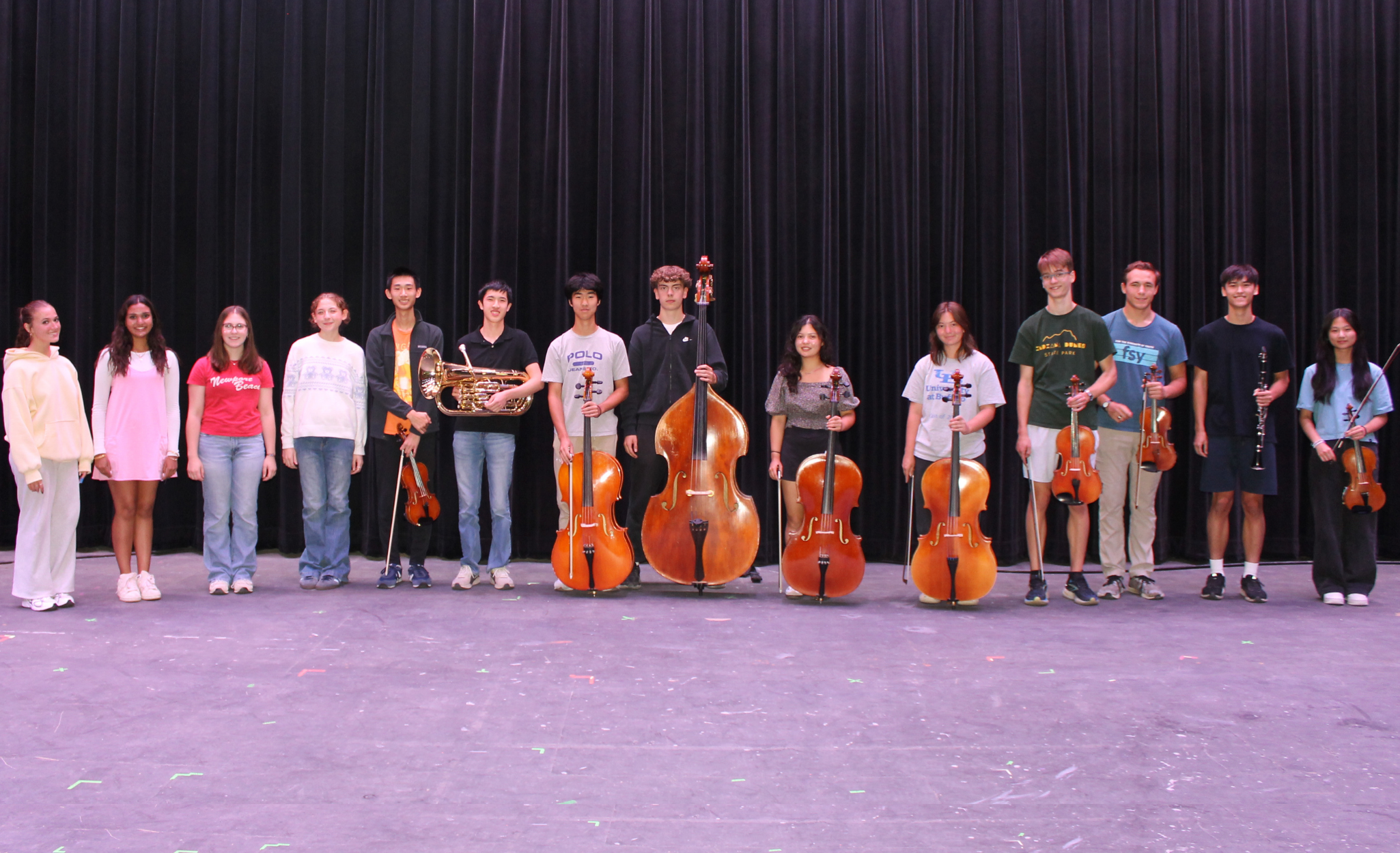 students standing side-by-side on a stage with some of them holding instruments
