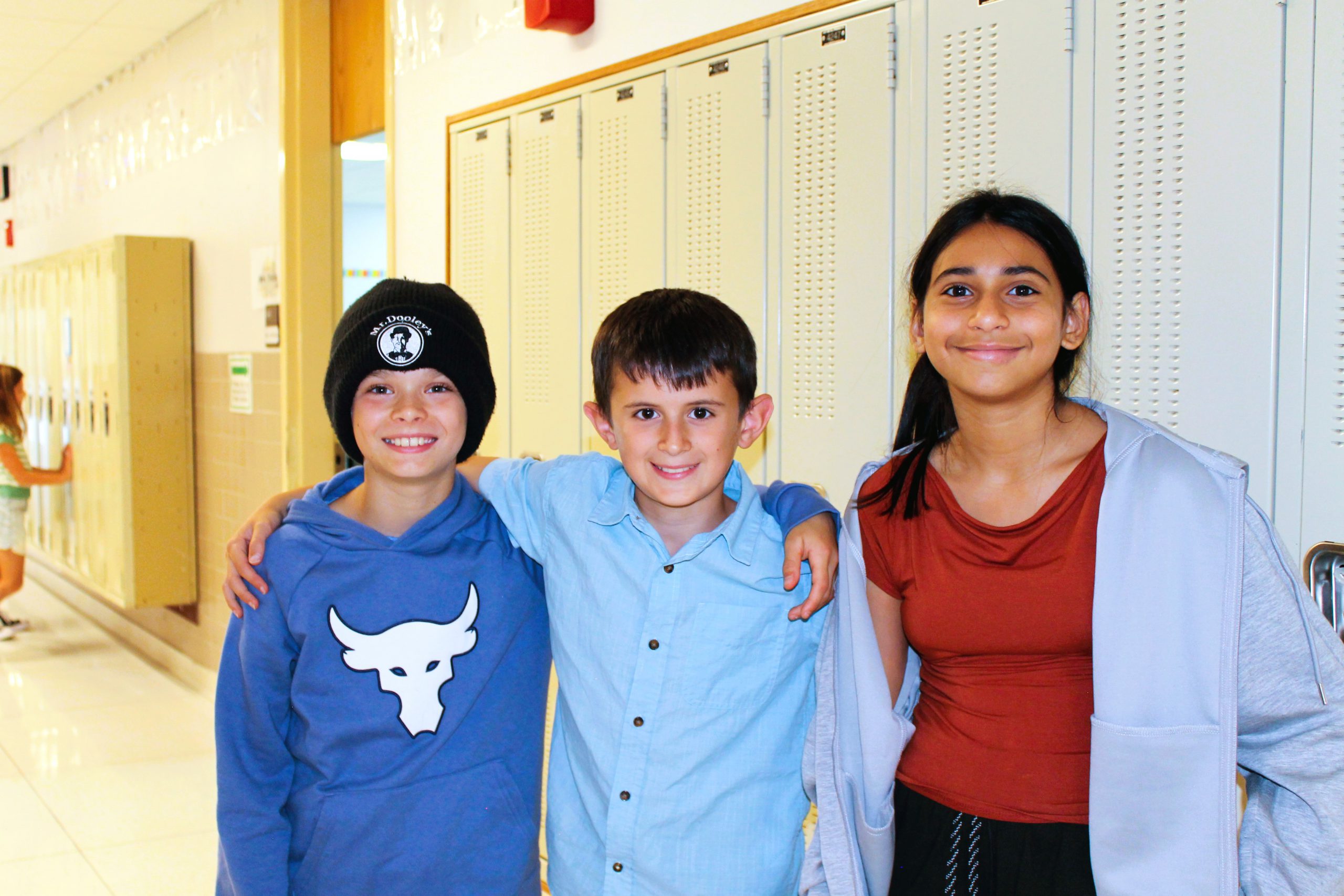 Three students pose for group photo in front of lockers.