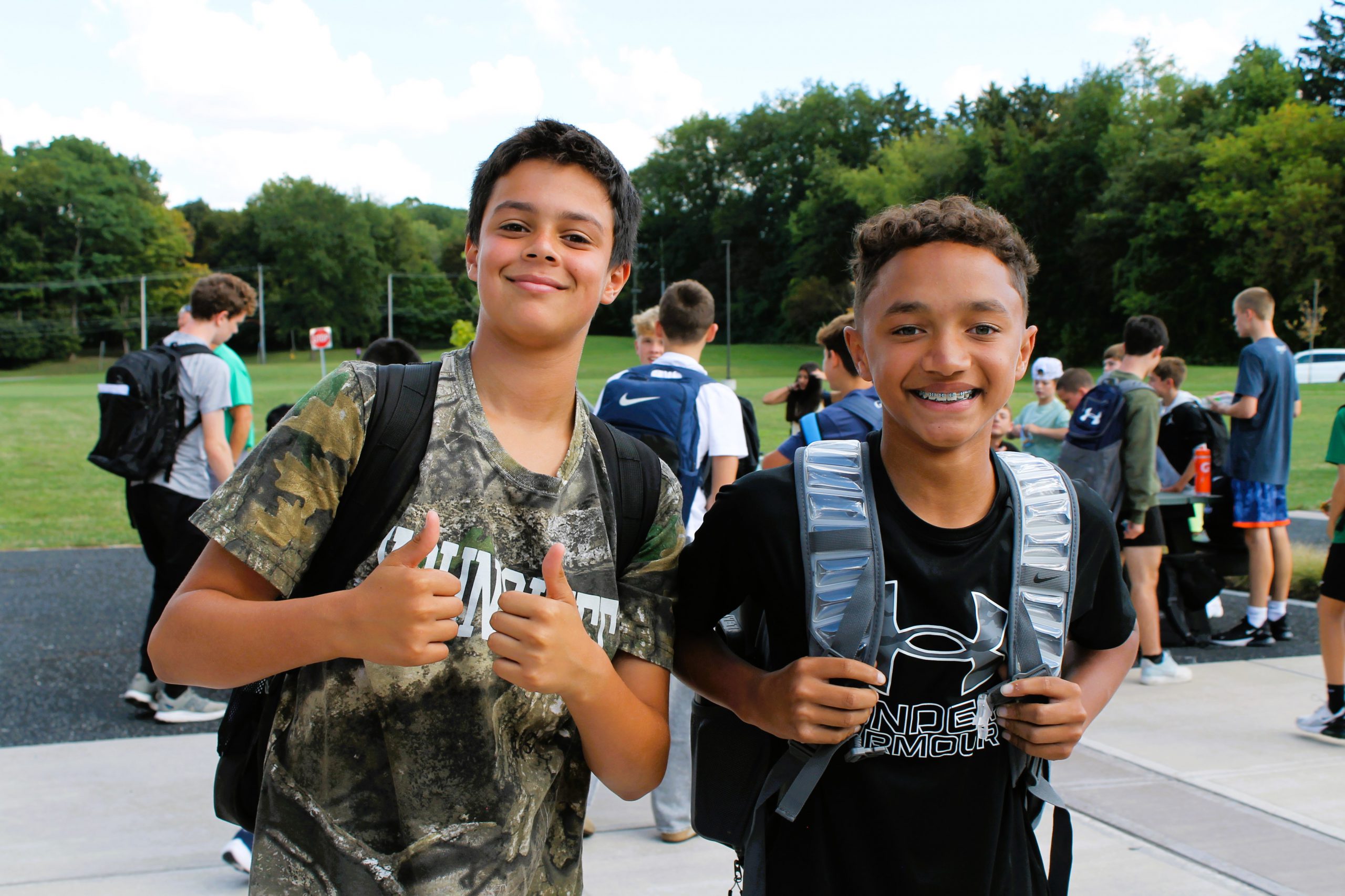 Two students pose for photo with smiles and thumbs up.