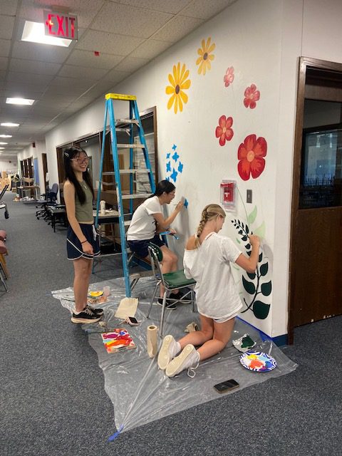 Students painting colorful flowers on a wall.