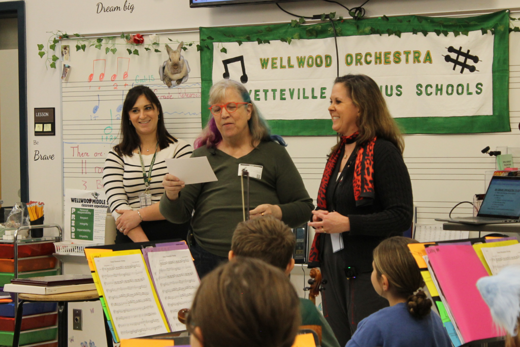 Three adults standing in front of an orchestra classroom with students