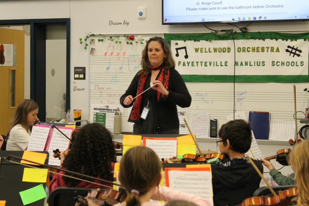 Amy Cirmo standing at the front of a classroom conducting orchestra students