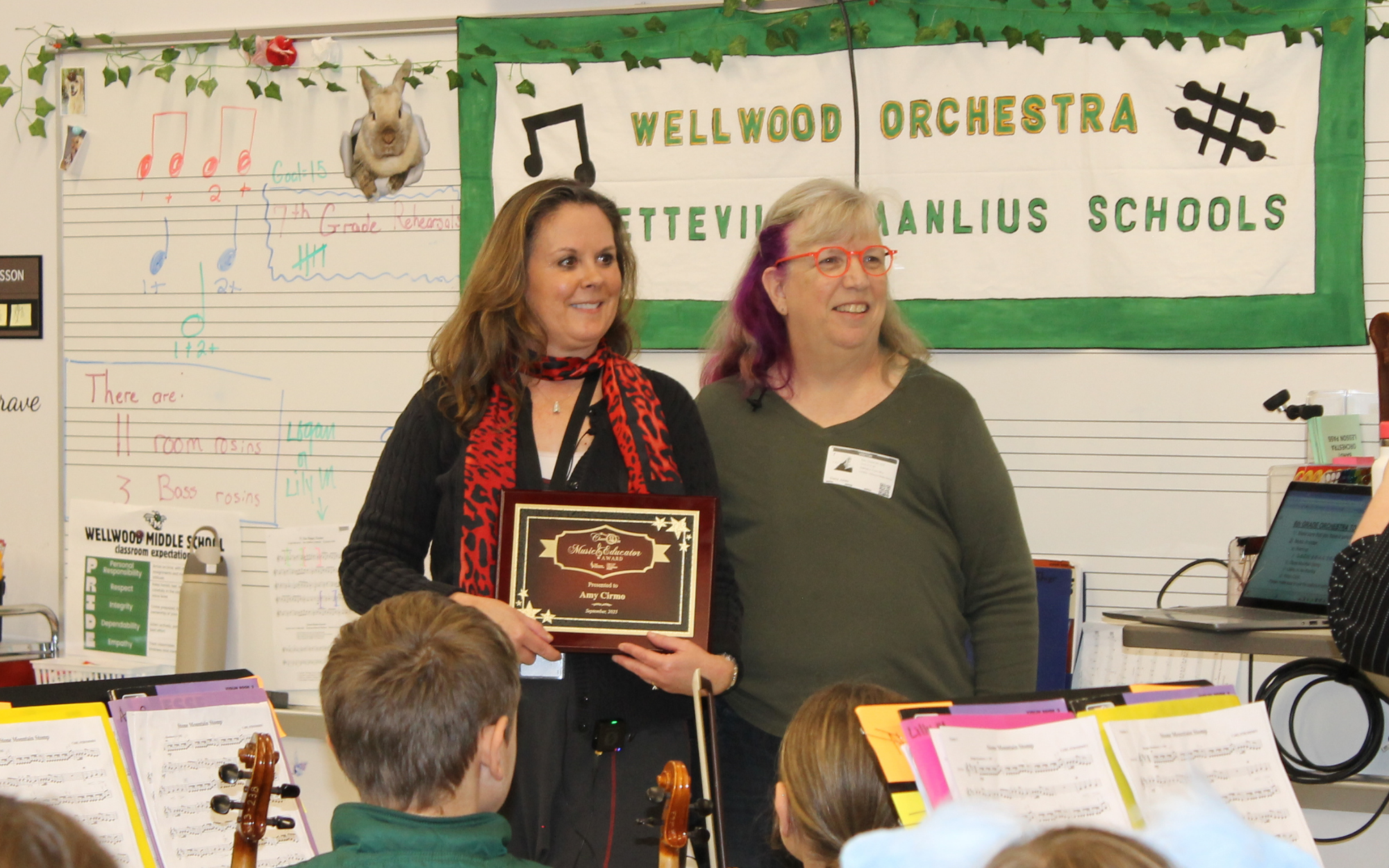 Amy Cirmo holding a plaque, standing alongside WCNY Classic FM Program Manager Diane Jones in front of a group of students