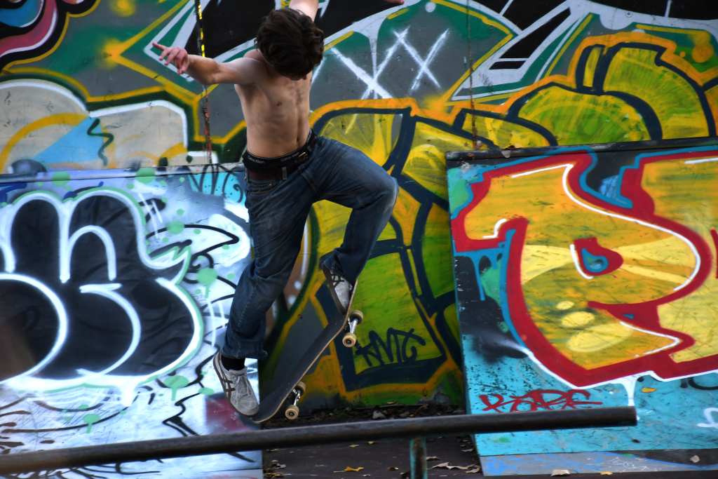 A teen boy skateboards, performing a trick in front of a graffiti wall.