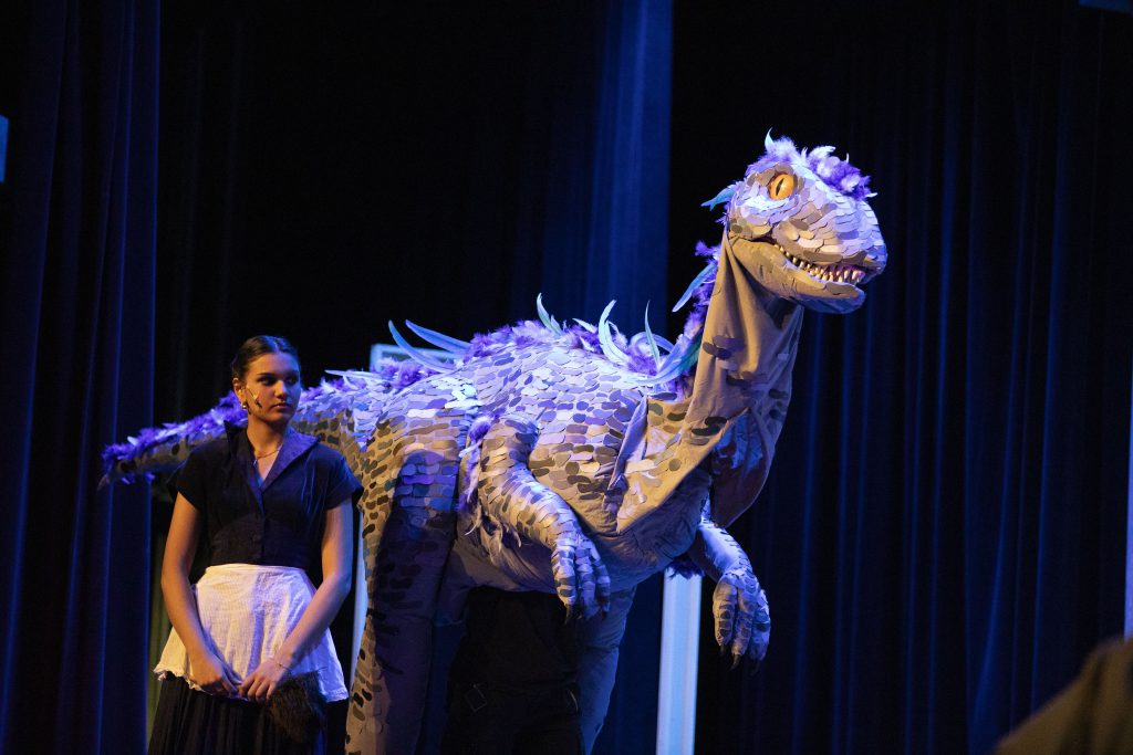 Dinosaur puppet and student performer on stage.