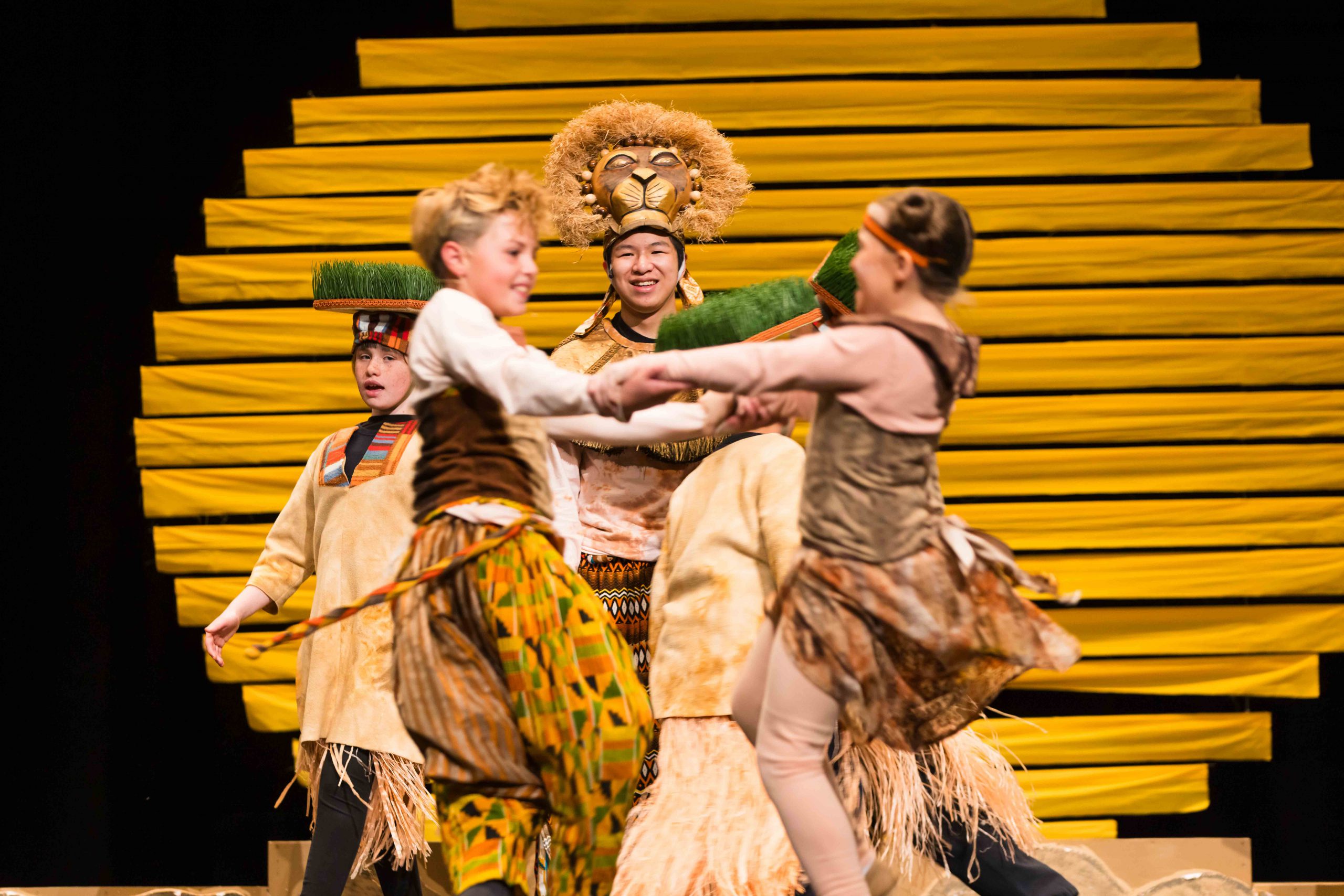 Students perform The Lion King Jr. on stage in costume.