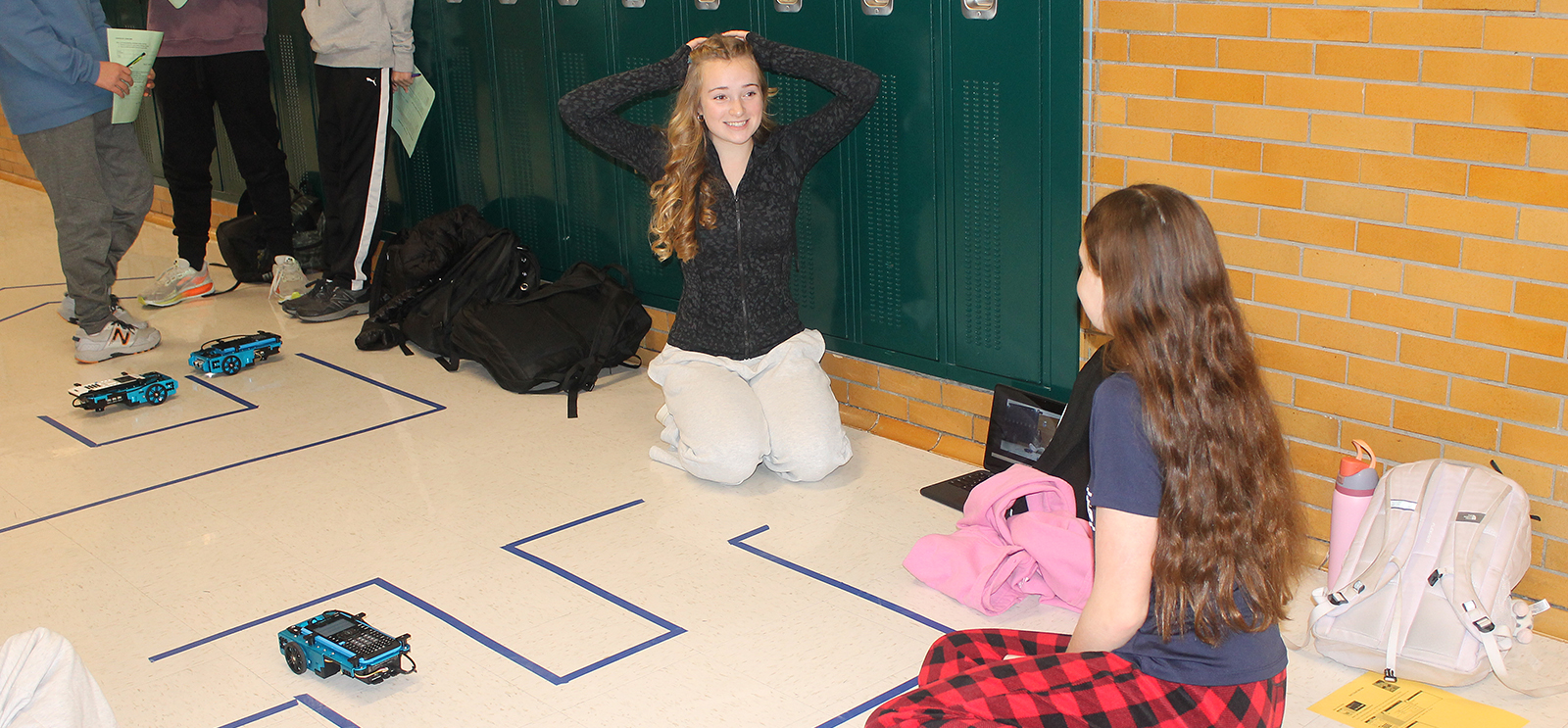 Girl sitting on floor with hands on top of her head, smiling, as a rover successfully navigates a maze.