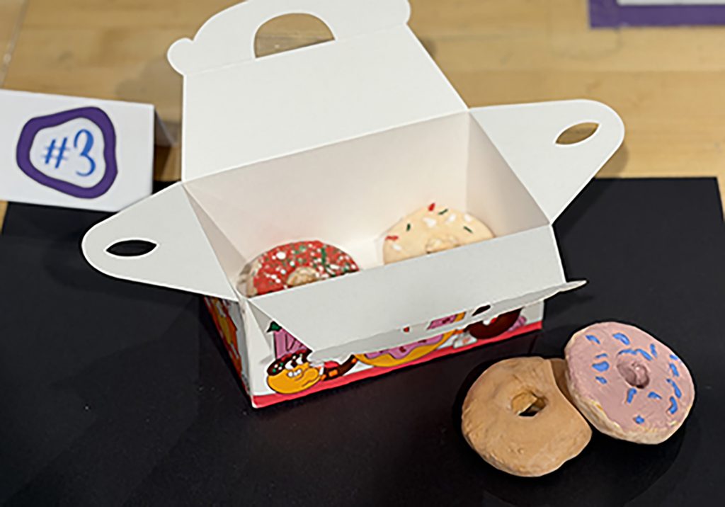 Sculpture of a box of donuts with two donuts on the table in front of the box