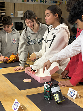 A group of students stand on one side of a table setting up their display for judges to review