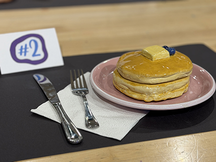 Clay sculpture of a stack of pancakes smothered in syrup with a pat of butter and blueberries on top