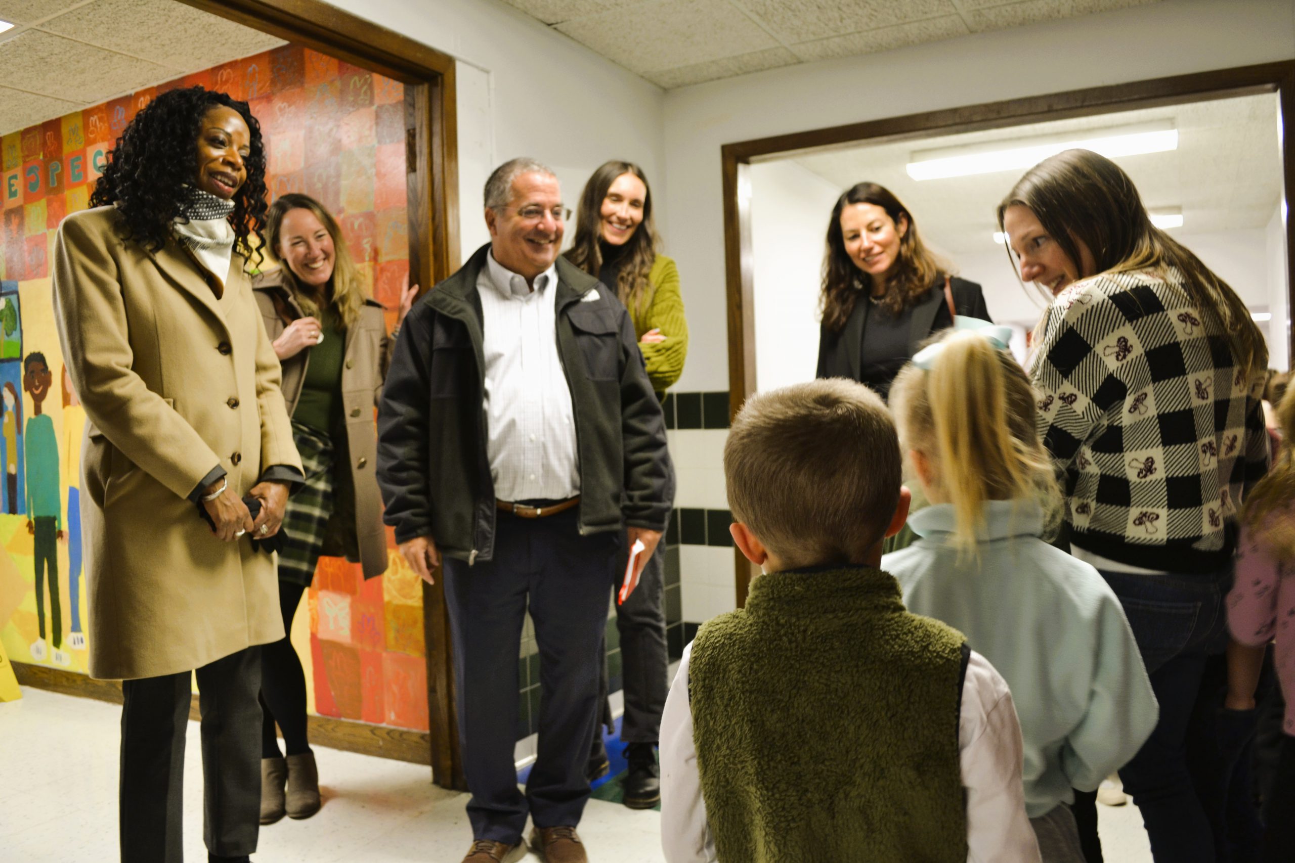 Magda Parvey and board members smile and speak with students and staff in hallway.