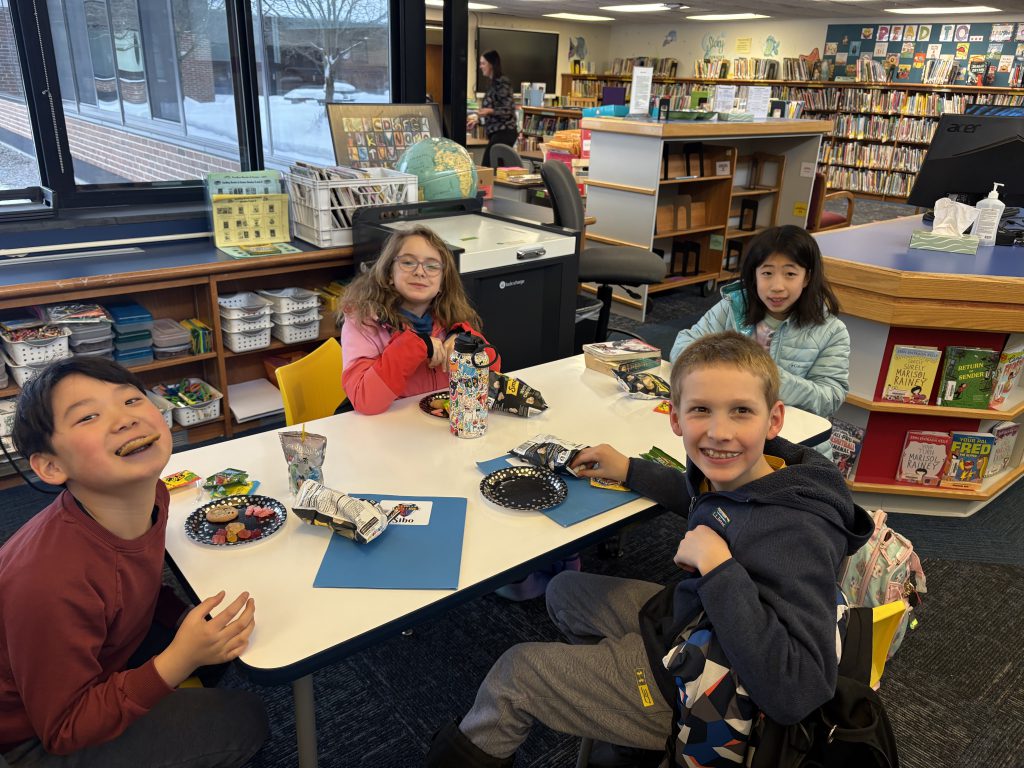 Fourth grade students smile at camera while sitting at library table.