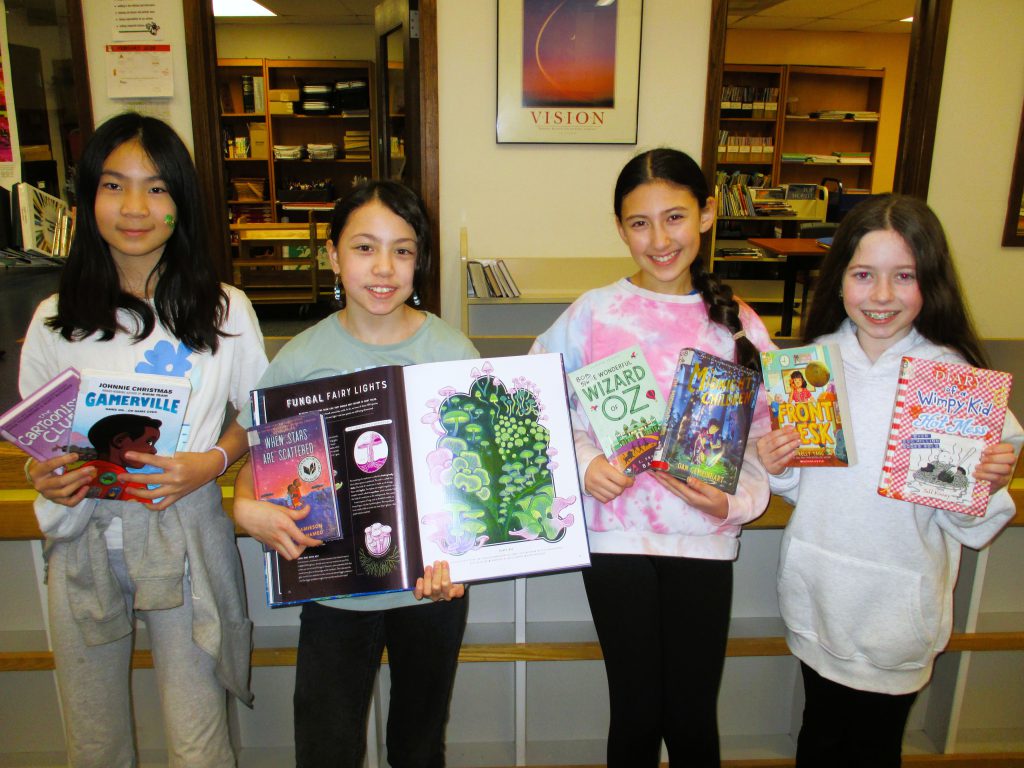 Four students pose with books smiling at camera.