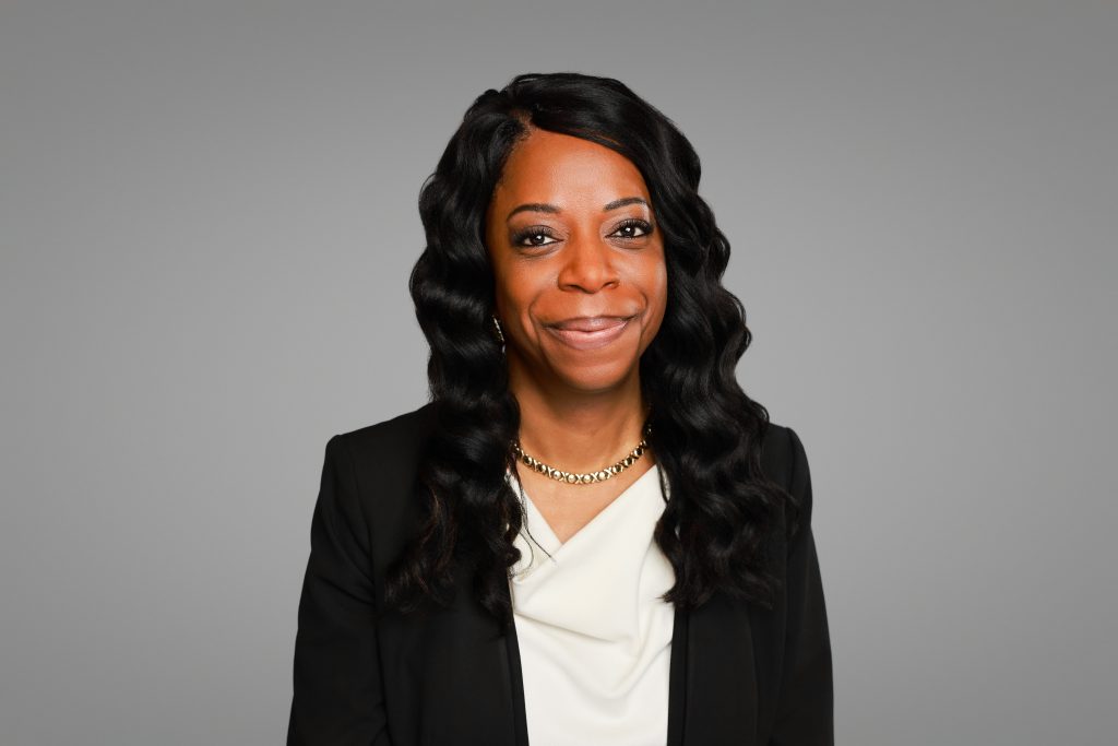 Woman with closed mouth smile poses in front of gray background.