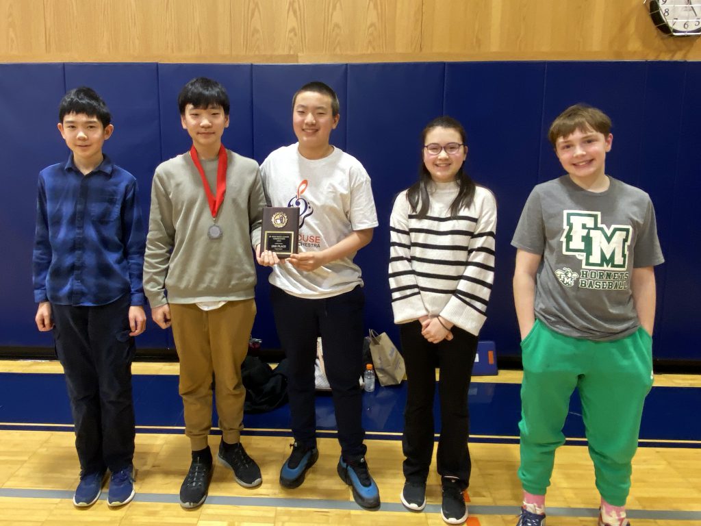 Five students pose for photo with blue gym mats behind them. 