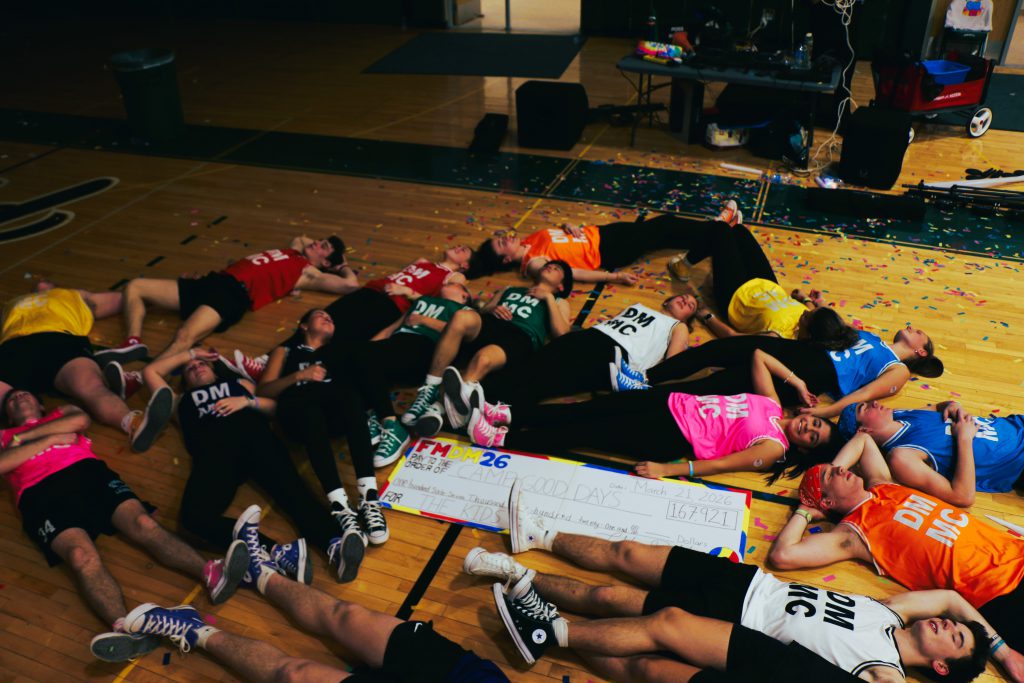 Students lay on gym floor around large donation check showing they are tired after the dance marathon.