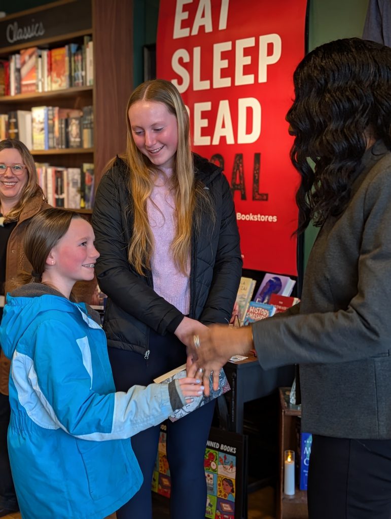 Dr. Parvey speaks with two girls at book shop. A woman smiles in the background.