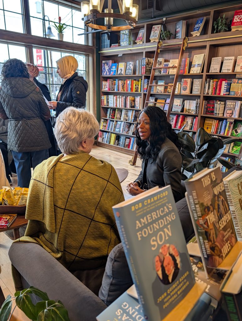 Dr. Parvey sits, speaking with a woman at meet and greet at book shop.