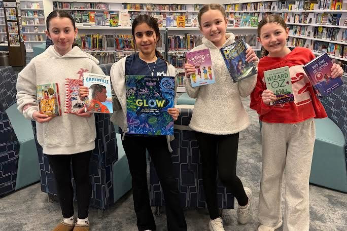 Four students standing in a row holding books 
