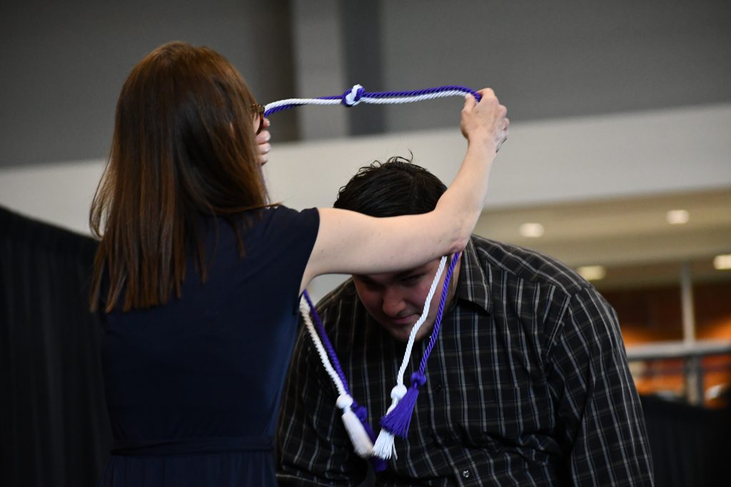 Student bends as a purple and white corded rope is placed over his head.