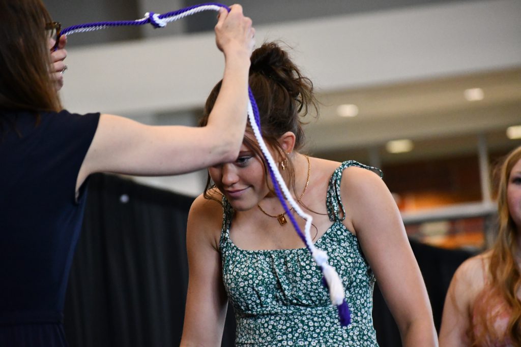 Student bends as a purple and white corded rope is placed over his head.