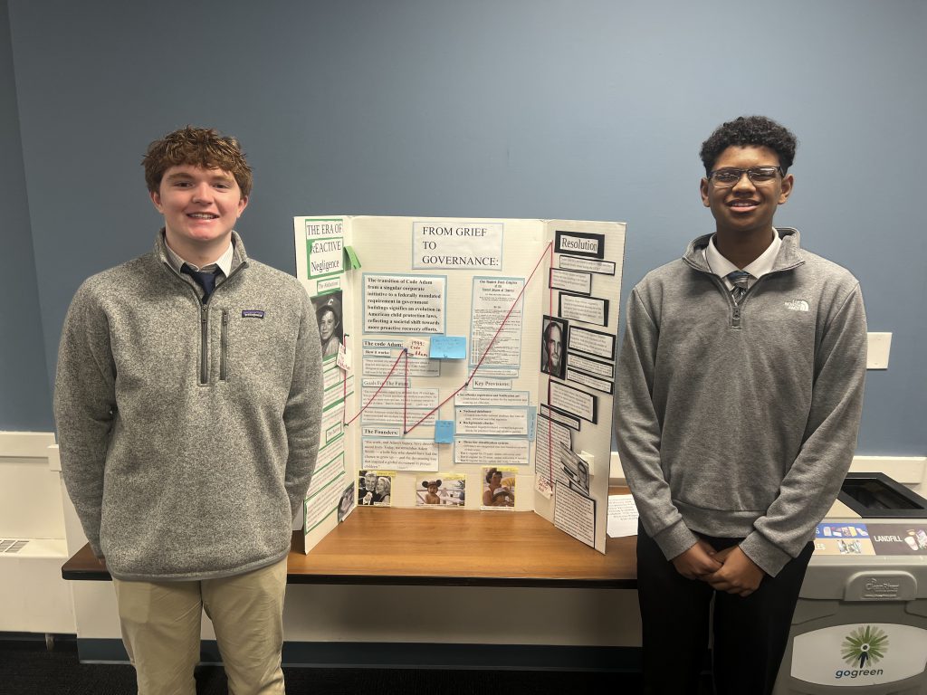 Two students stand next two tri-fold presentation board.