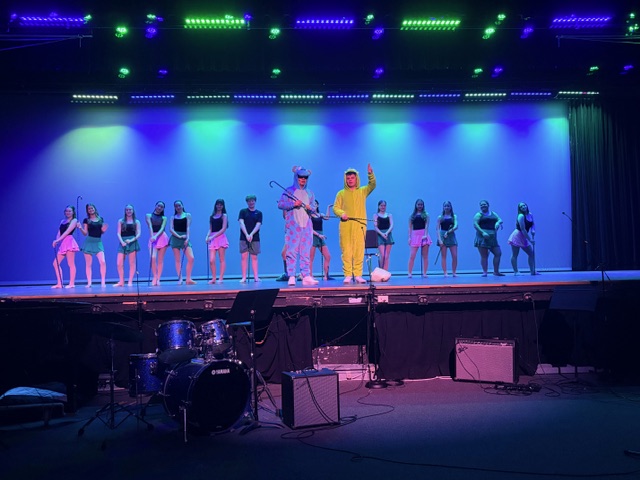 Two students wear Monsters Inc. costumes with a line of other performers standing in a line in the background.