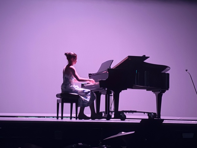 Female student sits at piano on stage.