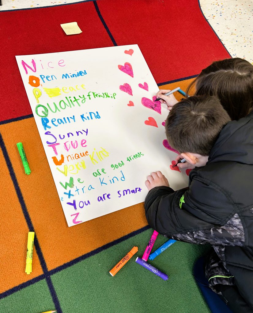 Two students draw hearts on poster on the floor.