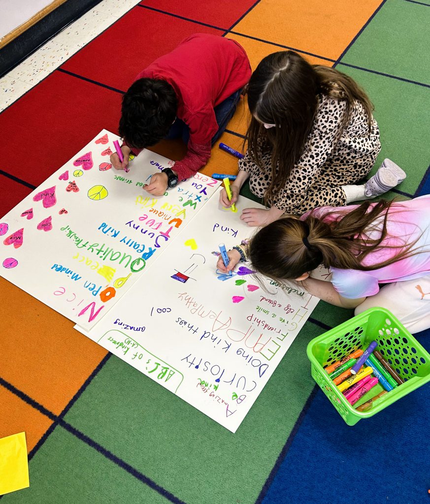 Three students draw hearts on poster on the floor.
