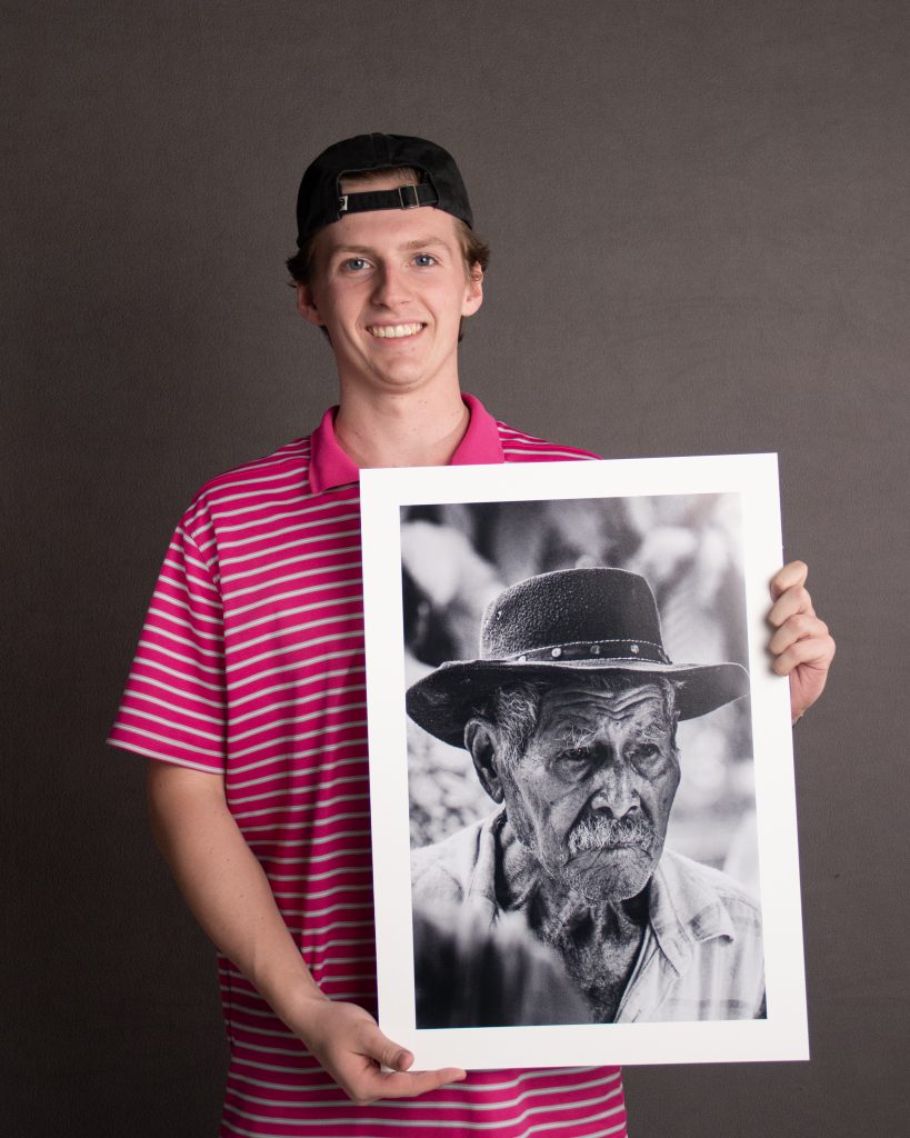 Student standing, holding a large photograph