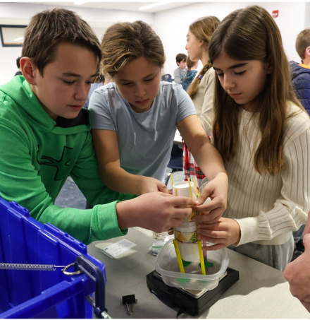 Three students work on project with cups and other items.