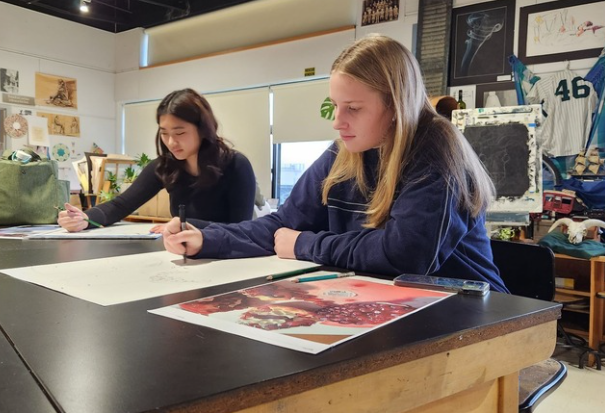 Two students sit at table while drawing.
