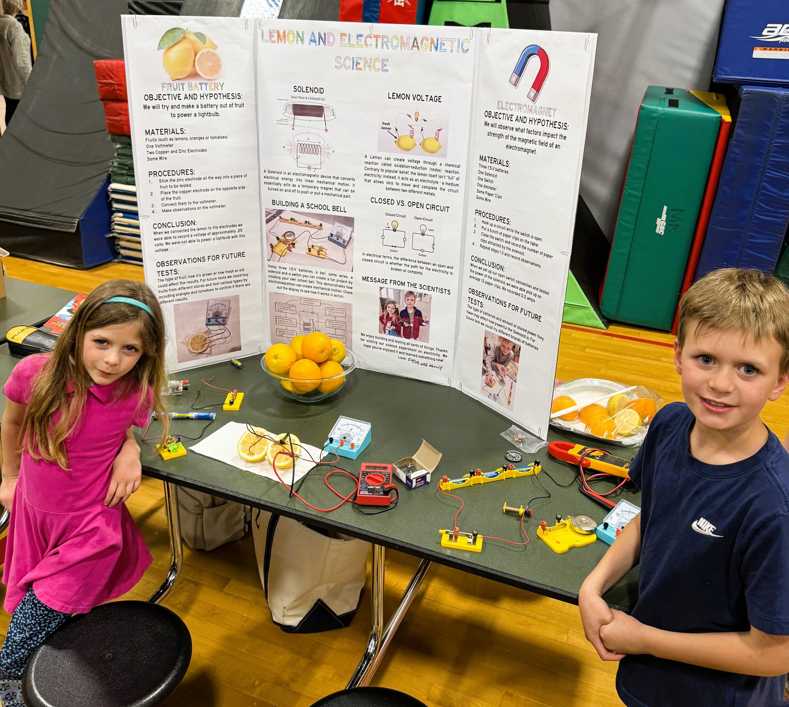 Two students stand next to tri-fold display at science fair.