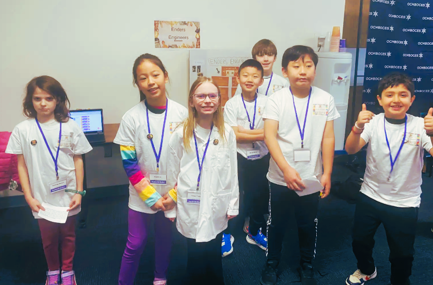 Group of students wearing white t-shirts and blue lanyards pose for group photo.