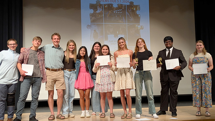 Students standing in a row on a stage, some holding certificates.