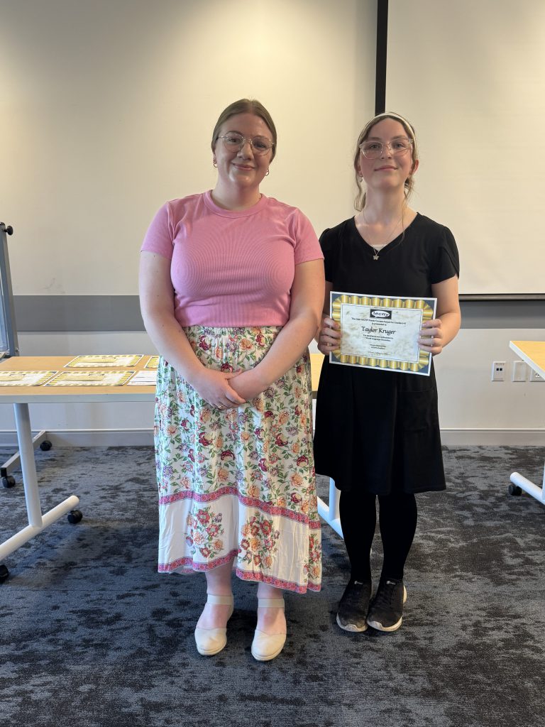 Taylor Krueger poses for photo with teacher while holding certificate.