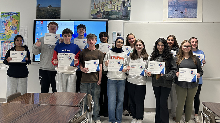 Students standing in a row, side by side in a classroom, holding paper certificates in front of them