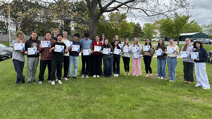 Students standing in a row, side by side, outside, holding paper certificates in front of them